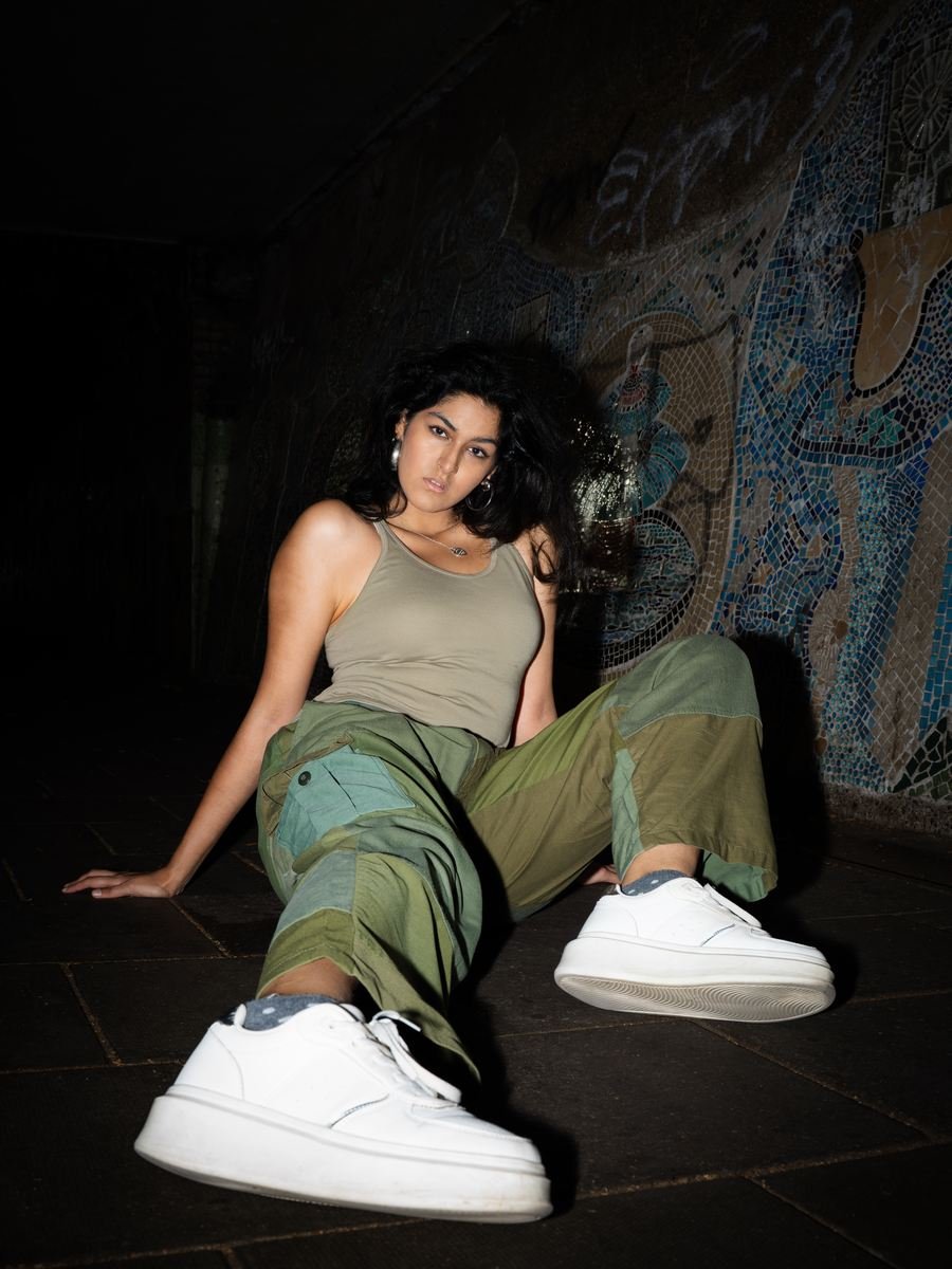 Flash portrait in an underpass, sitting low with white trainers toward the camera.